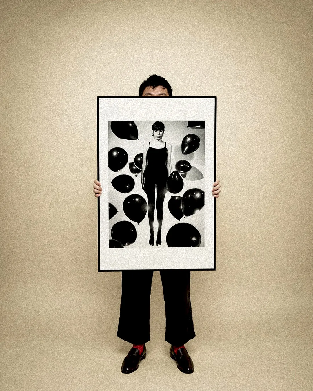 Lalo holding a framed black and grey print of a figure surrounded by balloons