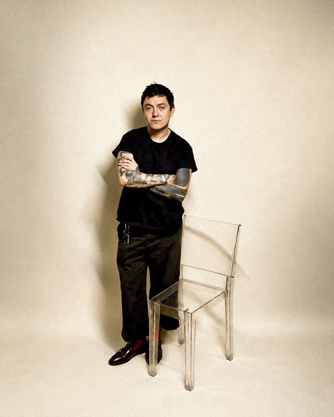 Lalo Domínguez, studio portrait leaning beside a clear ghost chair