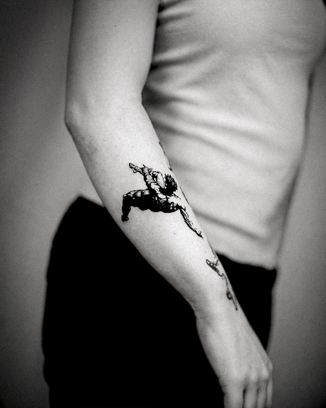 Woodcut tattoo of a falling winged figure on the forearm